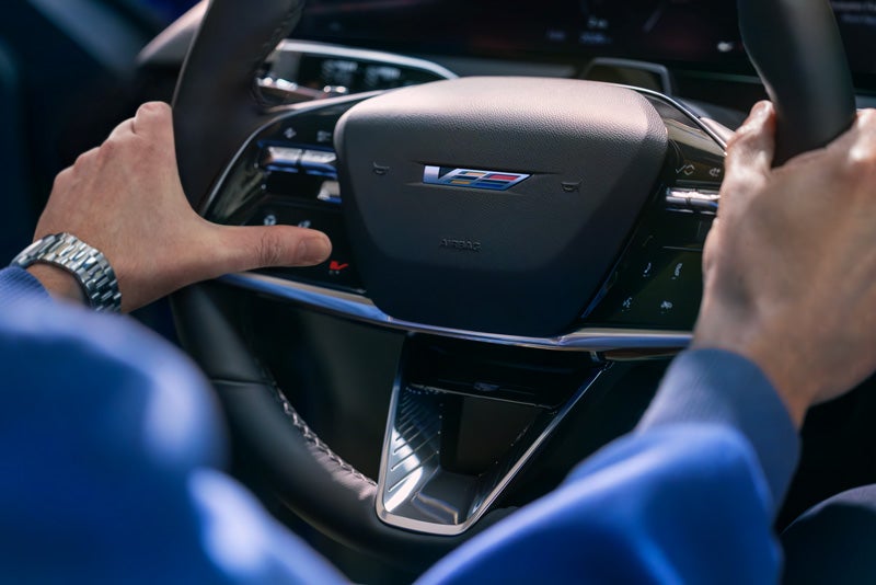 Close-up of a Man About to Press the V-Button on the 2026 OPTIQ-V Steering Wheel | Grand Island Cadillac in GRAND ISLAND NE