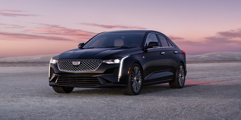 A sleek black Cadillac sedan is parked on an open landscape with a scenic sunset sky in the background, showcasing its modern design and signature LED headlights.